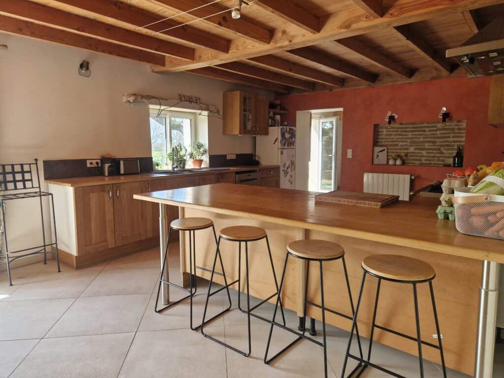 Une cuisine spacieuse et chaleureuse avec un grand îlot central en bois, des tabourets hauts et des poutres apparentes rustiques