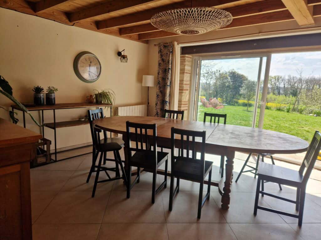 Salle à manger lumineuse avec grande table en bois ouverte sur le jardin