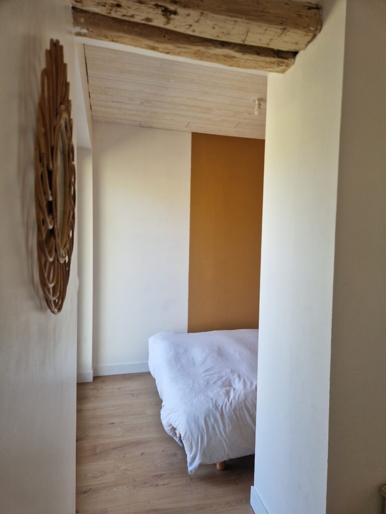Aperçu d'une chambre lumineuse et chaleureuse avec un lit douillet, des poutres apparentes et une décoration épurée pour un séjour reposant.