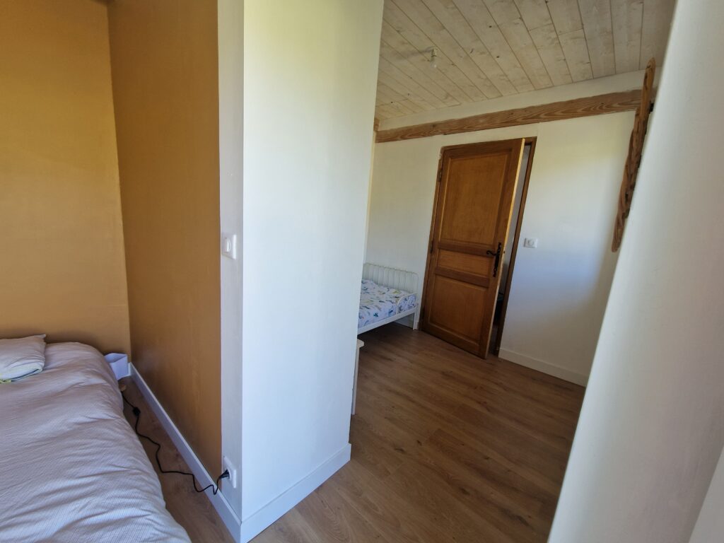 Cet espace nuit chaleureux propose deux lits séparés par une cloison, sous un plafond en bois authentique.