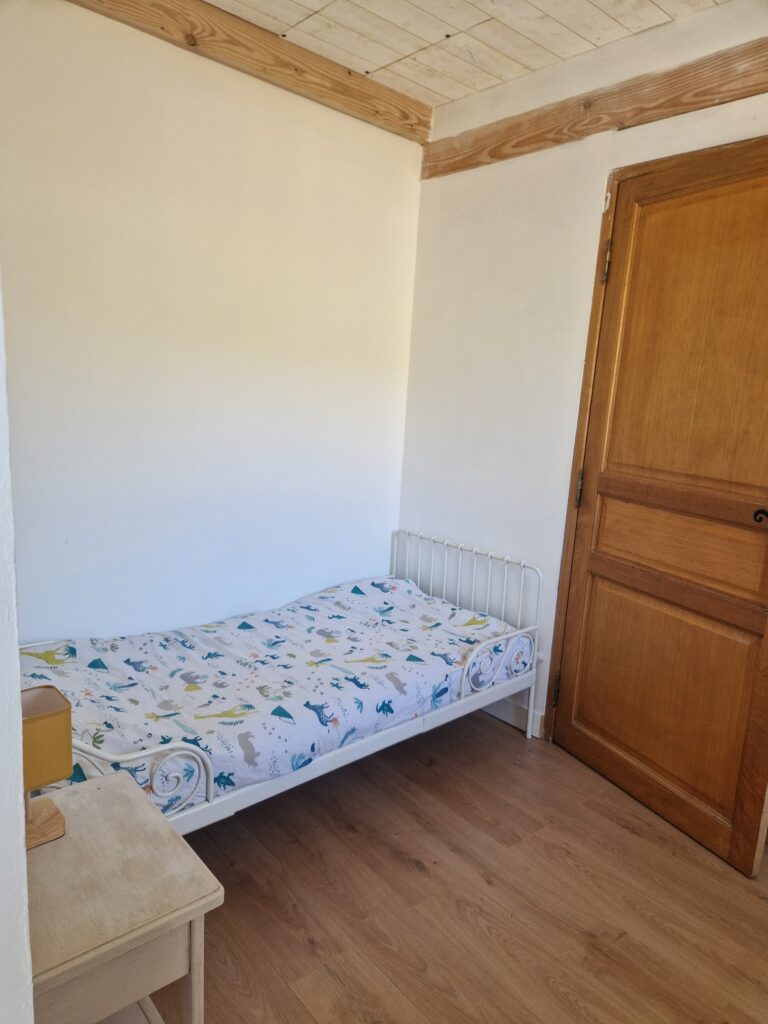 Une chambre d'enfant lumineuse avec un lit simple, des poutres apparentes et un parquet en bois chaleureux.