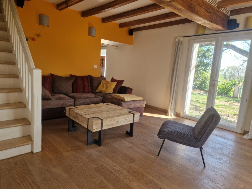 Salon chaleureux avec canapé, table basse en bois et accès jardin