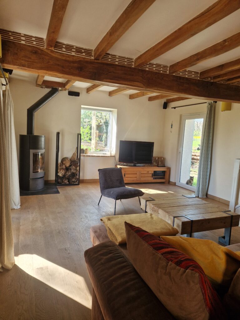Un salon chaleureux et lumineux avec des poutres apparentes, un poêle à bois et un mobilier confortable pour des moments de détente.