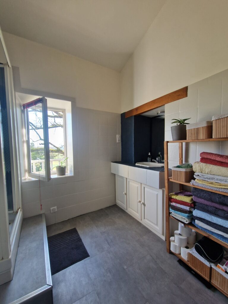Une salle de bain lumineuse et spacieuse avec un meuble vasque blanc, des étagères de rangement.