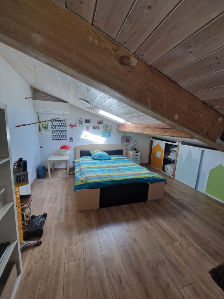 Une chambre mansardée chaleureuse avec un grand lit confortable, des poutres apparentes en bois et un parquet chaleureux.