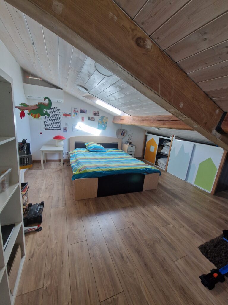 Une chambre mansardée chaleureuse avec parquet, poutres apparentes et un grand lit confortable