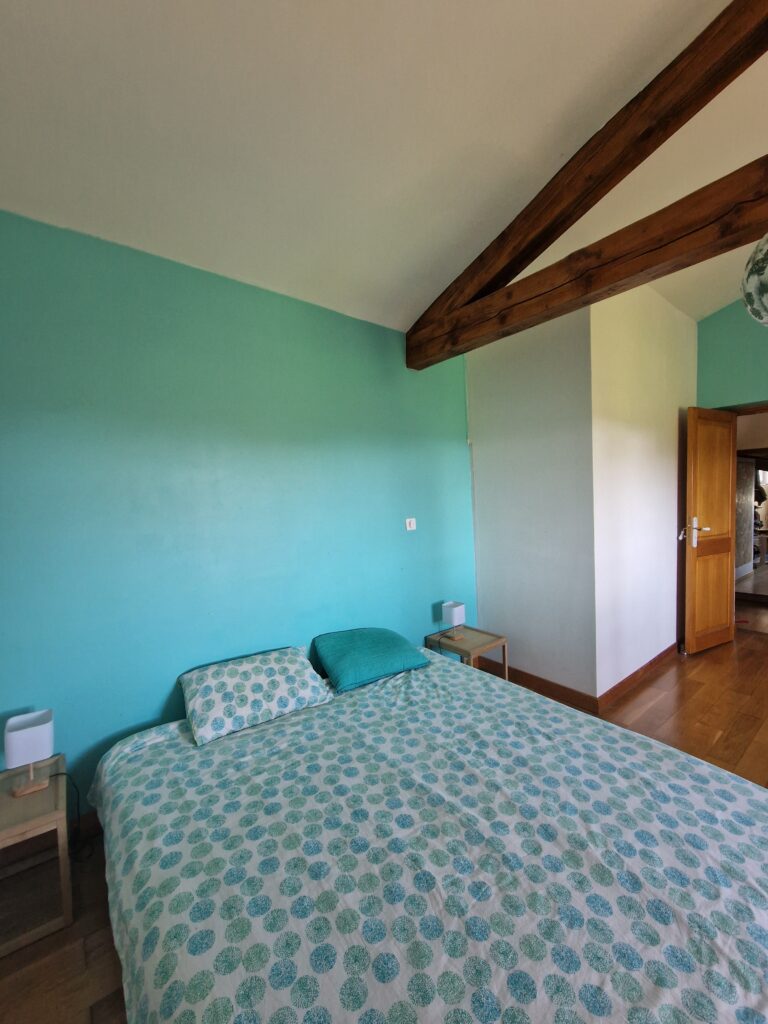 Chambre lumineuse avec mur turquoise et poutres apparentes